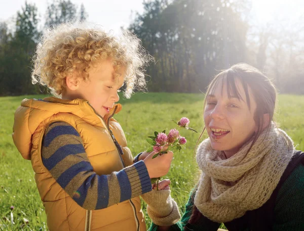 Niño en ropa de otoño le da a su madre una flor, primer plano — Foto de Stock