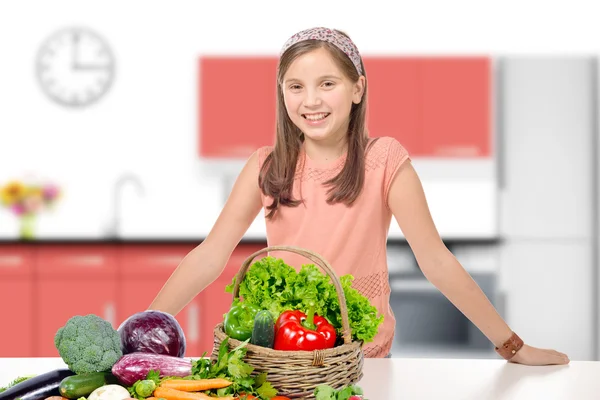 Leende ung flicka i ett kök, står bakom en hög vegetabl — Stockfoto