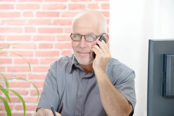 Middle aged businessman sitting at desk, with  phone — Stock Photo, Image
