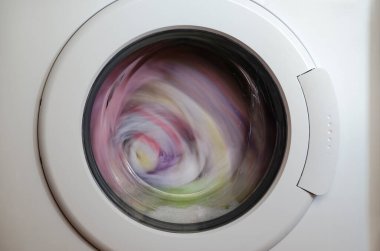 Çamaşır makinesi kapısı ve içinde dönen giysiler.