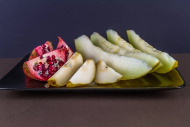 Nar kavunu ve armut dilimlenmiş ve tabakta sıralanmış. koyu arkaplan