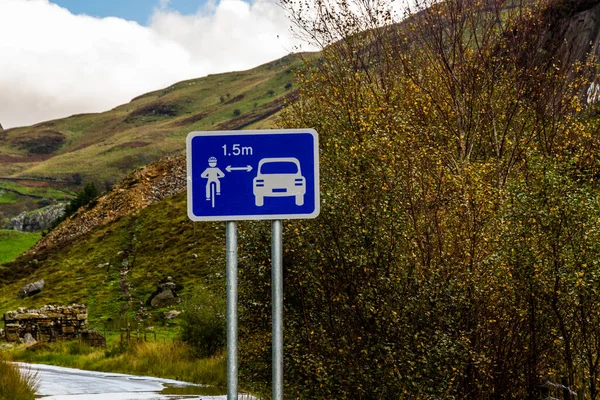 Sign in country of UK Wales. Showing car keeping 1.5 metres from cyclist, landscape.