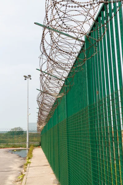 Arame farpado em cima da cerca verde que protege o terminal de ferry francês . — Fotografia de Stock