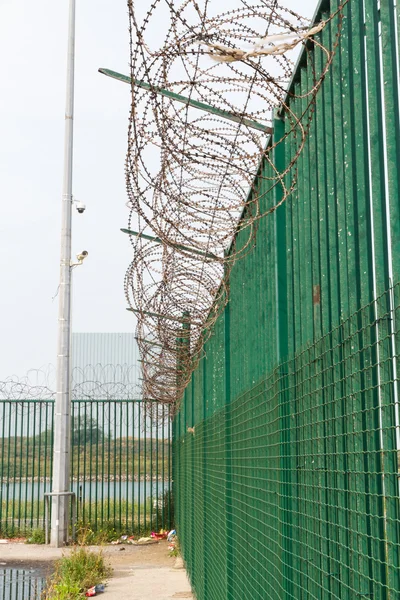 Arame farpado em cima da cerca verde que protege o terminal de ferry francês . — Fotografia de Stock