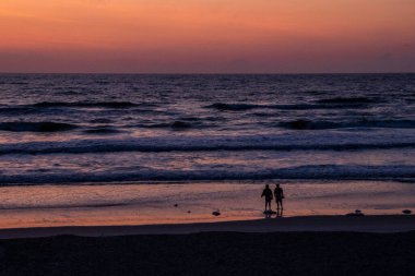 Güneşin doğuşunda sahilde iki kişi siluete büründü.