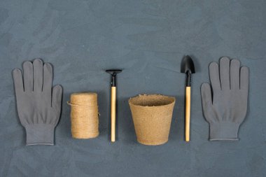 Eldivenli bahçe aletleri ve gri beton desenli arka planda çiçek dikmek için bir tencere. Yazı için uygun bir yer. Yukarıdan görüntüle.