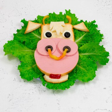 Funny sandwich with edible bull symbol of 2021 made of toast, sausage and egg on green lettuce leaves. Close-up. Breakfast idea for children. New Year, Christmas food, top view. holiday, holiday