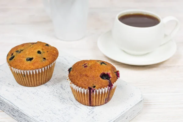 Delicious muffins with black currants close-up on a white wooden board on the background of a cup. — Stock Photo, Image