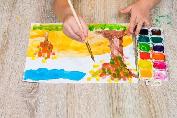 Dziecko rysuje jesienny penzage akwarelami. Zbliżenie dziecięcej dłoni pędzlem i akwarelami. Dzieci artysta rysuje, kreatywność, rekreacja, szkolenia, rysunek, kursy kolorów — Zdjęcie stockowe