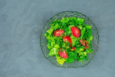 Yeşil yapraklar ve domates karışımından yapılmış yeşil vejetaryen salatası. Gri taş bir masanın üst görüntüsü.