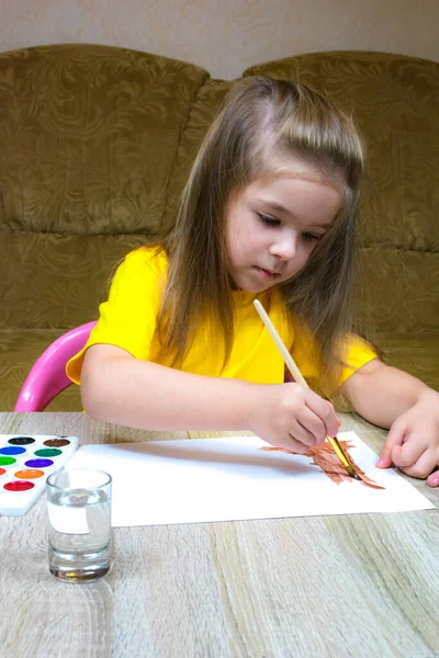 Een klein meisje in een geel T-shirt tekent een boomstam met aquarellen. — Stockfoto
