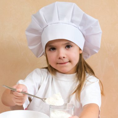 Aşçı gibi giyinmiş küçük bir kız hamuru yoğuruyor. Çocuk hayatı pişirme konsepti. Çocuk seviyor, eğleniyor, çalışıyor ve mutfakta oynuyor.