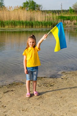Ukrayna bayrağı Ukraynalı küçük bir kızın ellerinde bir gölün ve sazlıkların arkasında dalgalanıyor. Ukrayna ve Bayrak Günü 'nün Bağımsızlık Günü.