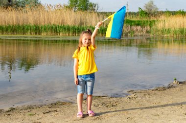 Ukrayna bayrağı gölün arka planına karşı küçük bir kızın ellerinde dalgalanıyor. Ukrayna ve Bayrak Günü 'nün Bağımsızlık Günü.