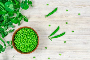 Yaprak filizlerinin arka planında taze yeşil bezelyeler, beyaz ahşap bir masada taze yeşil bezelyeler. Yukarıdan bak. Düzgün beslenme, vitaminler..
