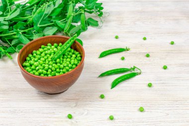 Yaprak filizlerinin arka planında taze yeşil bezelyeler, beyaz ahşap bir masada taze yeşil bezelyeler..