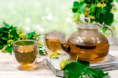 Cam çaydanlık ve iki bardak çay. Üzerinde ıhlamur ağacı olan ahşap bir masa, bulanık bir zemin ve ıhlamur yaprakları, çiçekler. Çay demliyorum..