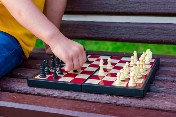 A girl plays chess in the park on a bench. Chess day. The childs hand rearranges the chess piece. Chess day. July 20.