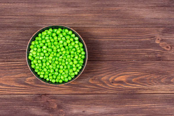 Verse groene erwten in een kom op een bruine houten tafel. Zicht van bovenaf. Plaats voor een opschrift. — Stockfoto