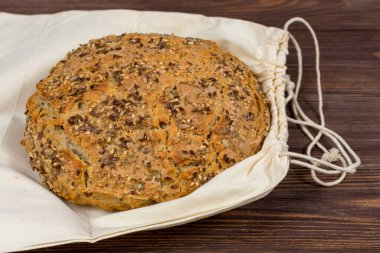 Beyaz bez torbada tahıl unuyla ev yapımı mayalı ekmek. Keten tohumu, susam tohumu, chia tohumu, ahşap bir masada ayçiçeği çekirdeği..