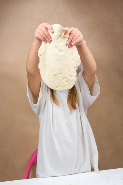 A little girl holds the dough by weight, covers her face. The development of fine motor skills in children. Salt dough modeling. — Stock Photo, Image