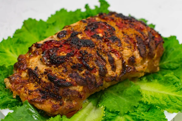 Een groot stuk gehakt varkensvlees, gekookt in de oven, gebakken in de oven, op groene sla bladeren, close-up. — Stockfoto