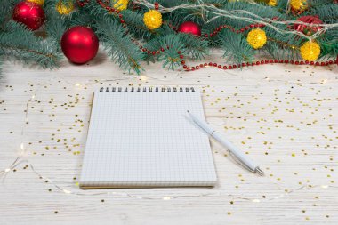 Beyaz bir masa üzerinde beyaz bir kalemle altın parıltılı boş bir defter oyuncaklarla süslenmiş bir Noel ağacının arka planında yıldızlar. Şenlik konsepti. Bir yazıt için yer.