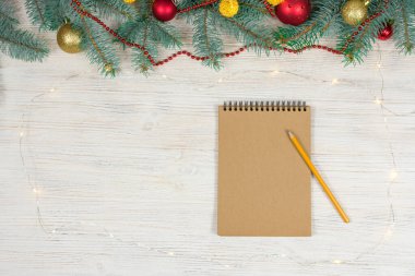Beyaz bir masa üzerinde beyaz bir kalemle altın parıltılı boş bir defter oyuncaklarla süslenmiş bir Noel ağacının arka planında yıldızlar. Şenlik konsepti. Bir yazıt için yer.