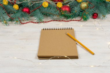 Beyaz bir masa üzerinde beyaz bir kalemle altın parıltılı boş bir defter oyuncaklarla süslenmiş bir Noel ağacının arka planında yıldızlar. Şenlik konsepti. Bir yazıt için yer.