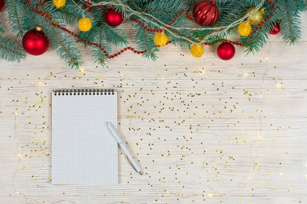 Beyaz bir masa üzerinde beyaz bir kalemle altın parıltılı boş bir defter oyuncaklarla süslenmiş bir Noel ağacının arka planında yıldızlar. Şenlik konsepti. Yazı için uygun bir yer. Yukarıdan görüntüle.