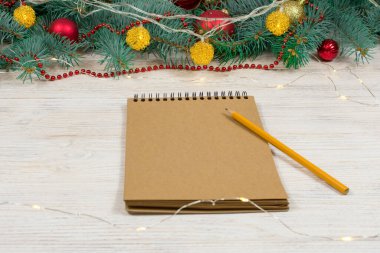 Beyaz bir masa üzerinde beyaz bir kalemle altın parıltılı boş bir defter oyuncaklarla süslenmiş bir Noel ağacının arka planında yıldızlar. Şenlik konsepti. Bir yazıt için yer.