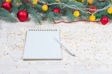 Beyaz bir masa üzerinde beyaz bir kalemle altın parıltılı boş bir defter oyuncaklarla süslenmiş bir Noel ağacının arka planında yıldızlar. Şenlik konsepti. Bir yazıt için yer.