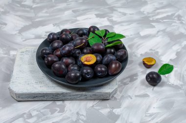 Taze olgun erik meyveleri bir kase içinde doğranmış ve tahta kesme tahtasının üzerinde taş beton arka planda. Yakın plan..