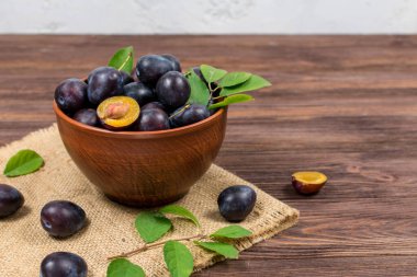 Taze olgun erikler kahverengi ahşap bir masada çuval bezi hasırları üzerinde bir kasede yapraklarla dilimlenmiş. Yaz hasadı.