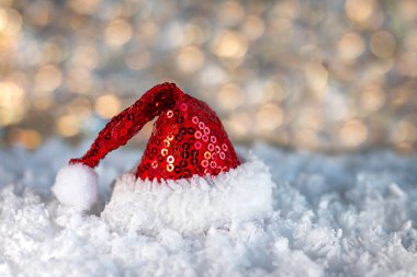 Kırmızı pullu Noel Baba şapkası yumuşak kar üzerinde oturur ve yumuşak bokeh ışığıyla neşeli, sıcak bir tatil sahnesi yaratır..
