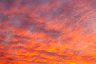Turuncu ve pembe bulutlu kızgın günbatımı gökyüzü dramatik, sıcak ve sakin bir hava yaratıyor..