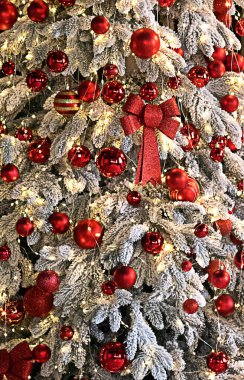 Snowy evergreen tree adorned with red baubles, glittering bow, and twinkling fairy lights for festive cheer.
