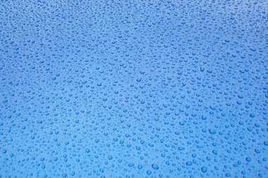 Su damlacıklarıyla lekelenmiş pürüzsüz mavi yüzey parlak ve soyut bir arkaplan oluşturuyor.