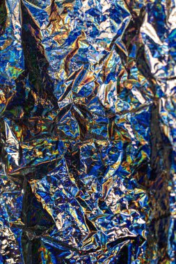 Kırışmış metalik folyonun mavi, yeşil ve altın tonlarında parlak yansımaları olan yakın plan görüntüsü.
