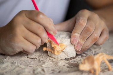 Hamurla el işi yapan bir çocuk süslü bir bloktan küçük bir turuncu dinozor oyuyor..