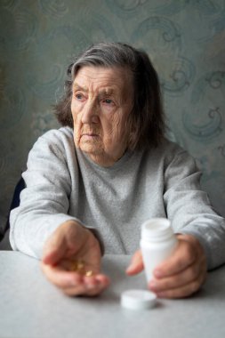 Evde elinde ilaç şişesi ve kapsüller tutan düşünceli yaşlı bir kadın yaşlanma, yalnızlık ve sağlık sorunları taşıyor..