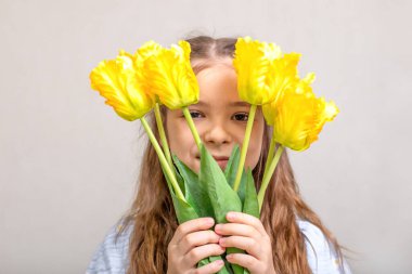 Genç kız, parlak sarı bir lale buketinin arkasından bakar. Baharı, masumiyeti ve neşeyi çağrıştırır..