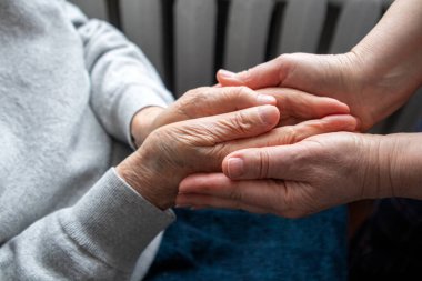 Bakıcı yaşlı bir insanın elini nazikçe tutar, destek, güven, rahatlık ve insan ilişkileri sağlar..