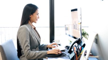 Asyalı kadın ofis masasında çalışmak için bilgisayar kullanıyor. 