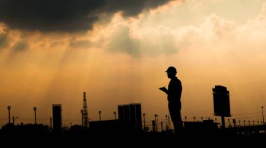 Mühendis, gün batımı siluetinde inşaat alanında dijital tablet kullanıyor