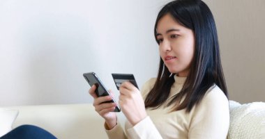Kanepede oturan ve online alışveriş için akıllı telefon ve kredi kartı kullanan bir kadın.