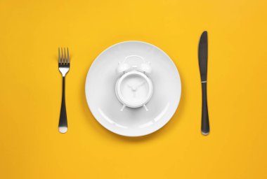 Çatal ve bıçaklı bir tabakta çalar saat.