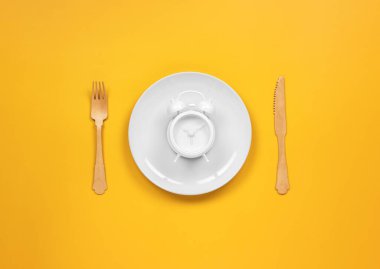 Çatal ve bıçaklı bir tabakta çalar saat.