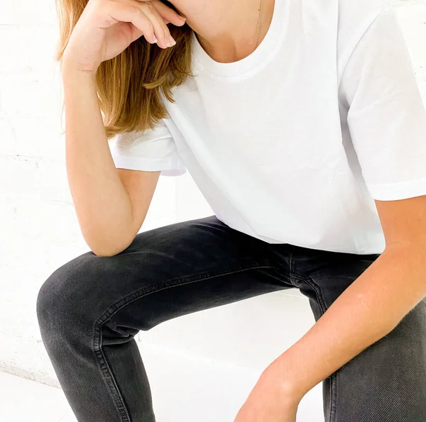 Schöne junge Frau in weißem T-Shirt und schwarzen Jeans sitzt auf der Treppe — Stockfoto