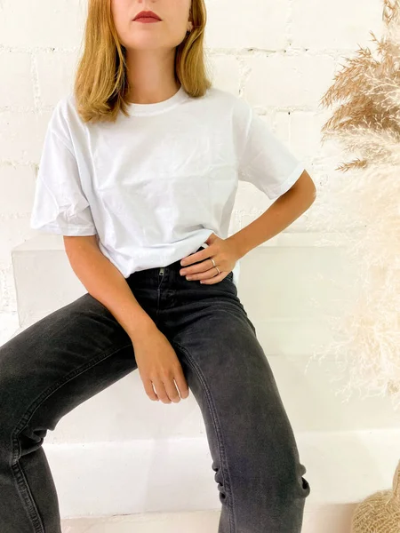 Schöne junge Frau in weißem T-Shirt und schwarzen Jeans sitzt auf der Treppe — Stockfoto